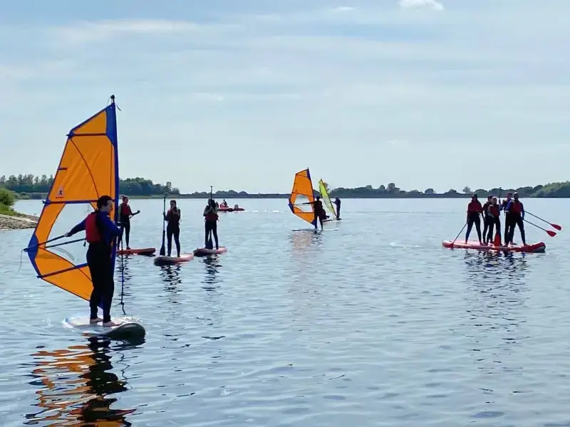 A mix of windsurfers and paddleboarders on a sunny day
